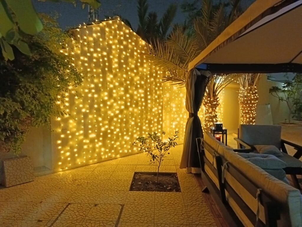 bright yellow curtain lights covering an exterior villa wall, lighting up a tiled outdoor area.