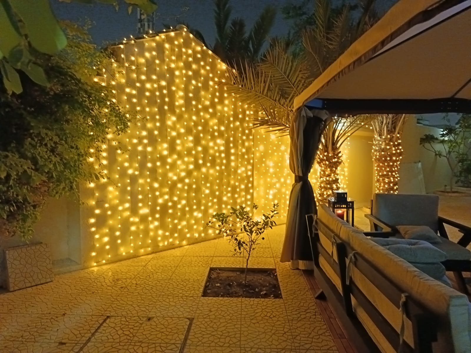 Home bright yellow curtain lights covering an exterior villa wall, lighting up a tiled outdoor area.