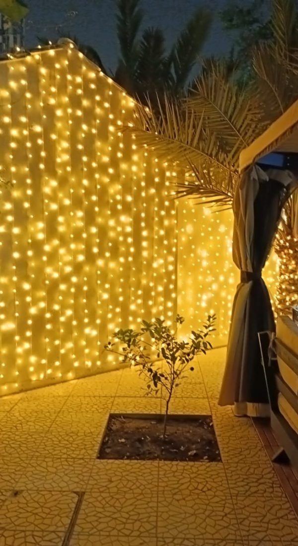 bright yellow curtain lights covering an exterior villa wall, lighting up a tiled outdoor area.