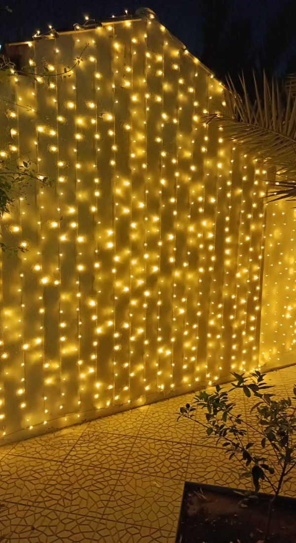 tall villa wall fully covered with dense golden curtain lights, creating a glowing backdrop at night.